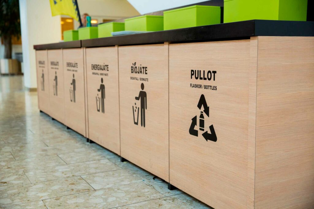 Kuvassa näkyy ravintolassa puisia kierrätysastioita erilaisille jätetyypeille, kuten pullot, biojäte ja energiajäte.