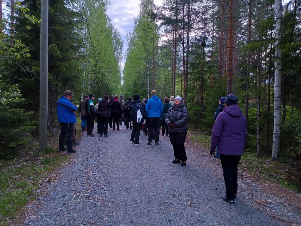 Joukko ihmisiä linturetkellä metsätiellä.
