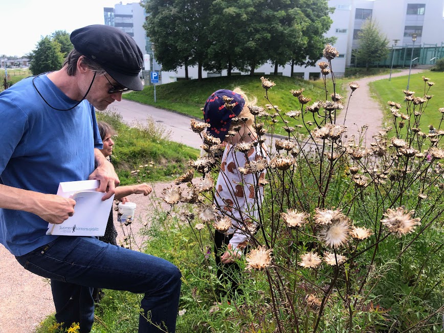Aikuinen ja lapsi keräämässä siemeniä kirjekuoreen luonnonkukkien keskellä.