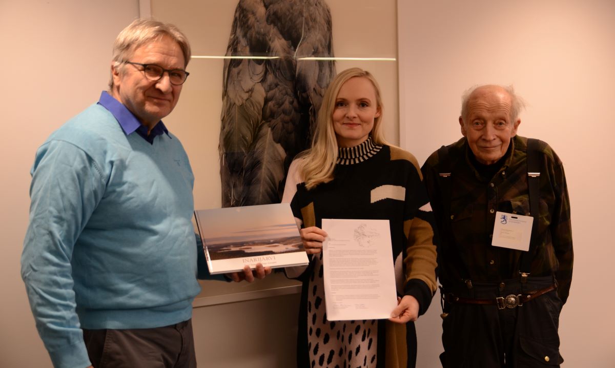 Ilkka Roininen ja Harald Helander poseeraavat Maria Ohisalon kanssa sisätiloissa. Ohisalolla on kädessään kansallispuistoaloite.