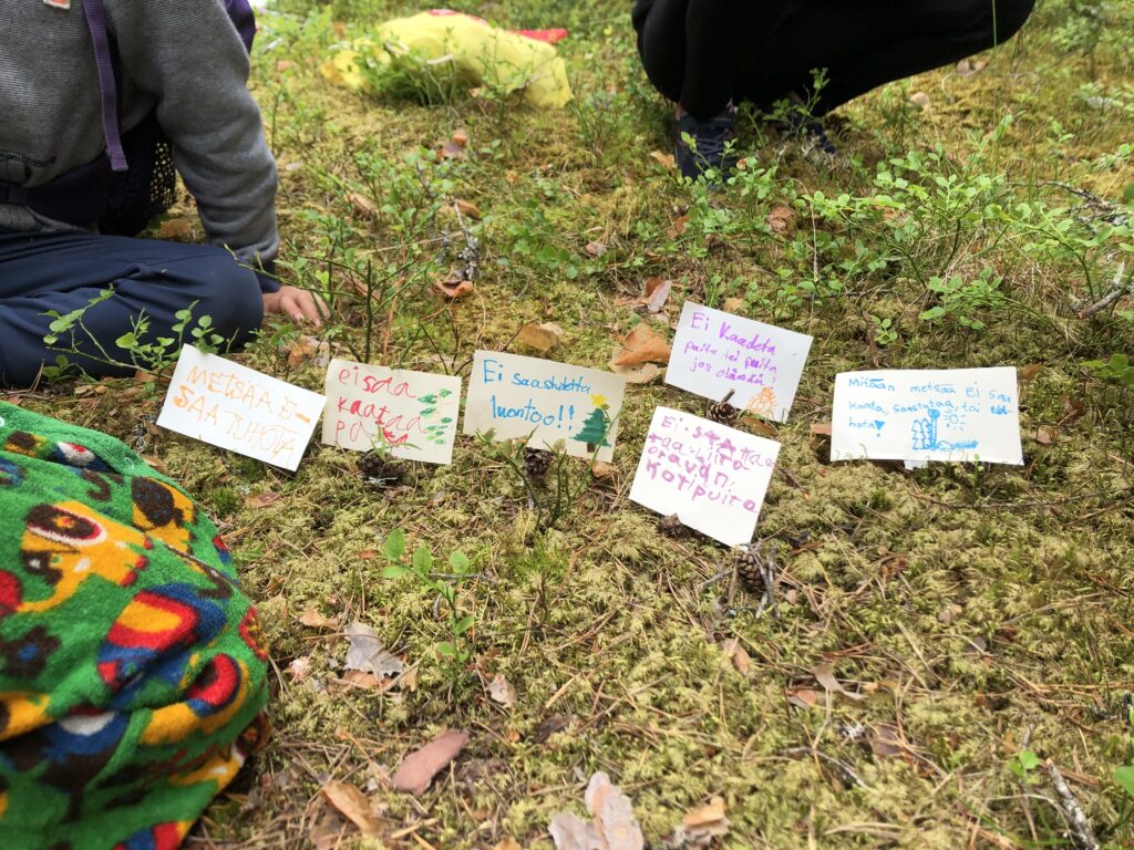 Lasten tekemiä minimielenosoituskylttejä, joissa vaaditaan metsän suojelua ja roskaamisen lopettamista.