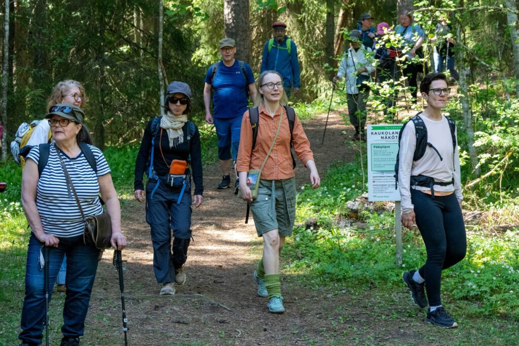 Oranssiruutupaitainen retken opas Riina kävelee retkeläisten keskellä metsäpolulla.