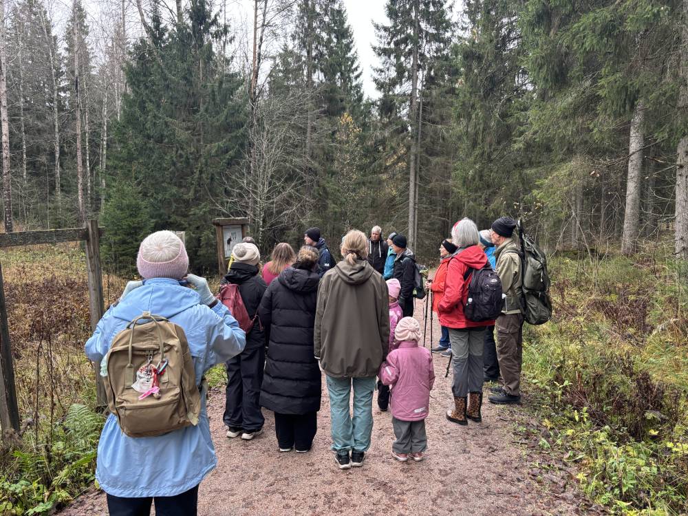 Människor står vid en infortavla i skogen på hösten.