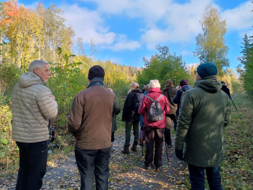 Retkeilijäryhmä syksyisellä metsäpolulla, jonka reunoilla näkyy ruskan värittämiä puita.