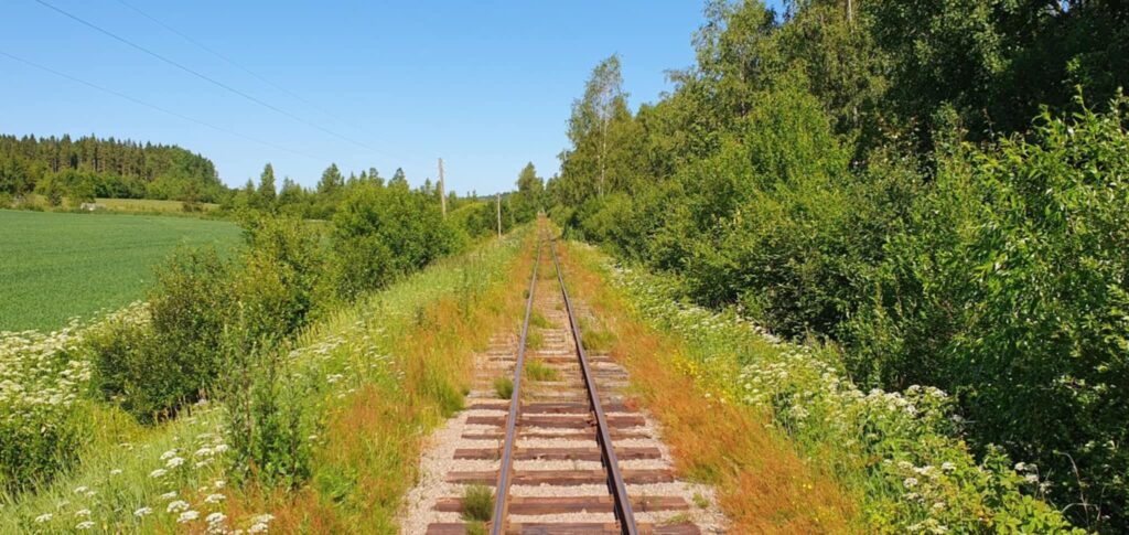 vanha kapearaiteinen junarata kesäisessä peltomaisemassa.