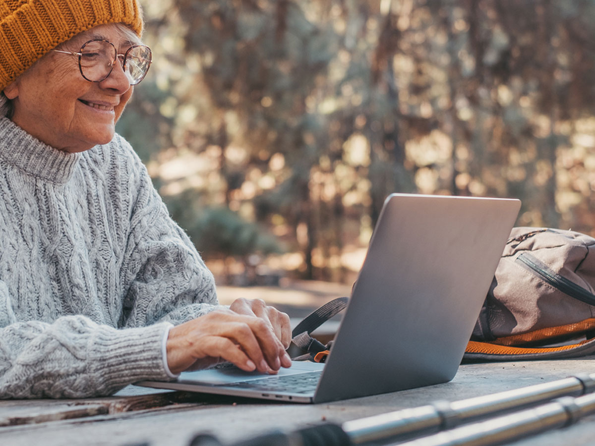 Retkeilijä taukopaikalla tietokoneen äärellä ja luonnon ympäröimänä.