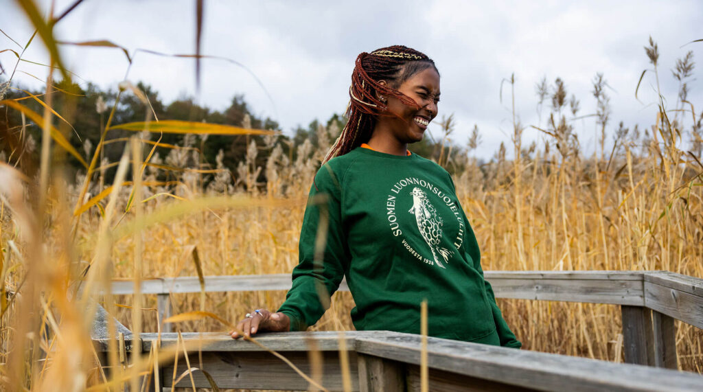 Norppapaitainen henkil&ouml; ulkoilemassa kaislikkomaisemassa.