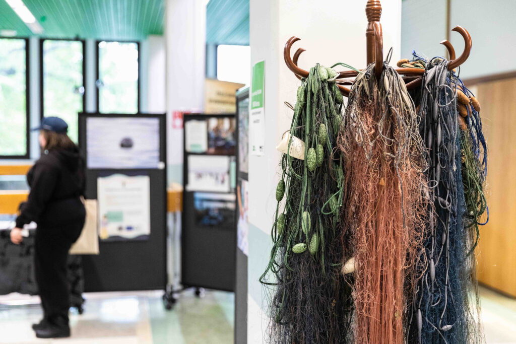 Vanhoja kalaverkkoja roikkuu naulakossa, taustalla ihminen tutustuu näyttelyyn.