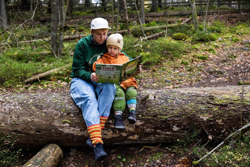Aikuinen ja lapsi istuvat puunrungolla ja lukevat yhdess&auml; kirjaa.