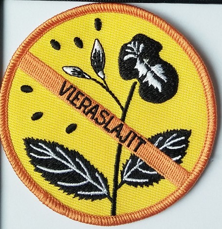 Haalarimerkki, jossa kieltomerkin takana jättipalsami. Haalarimerkissä lukee "Vieraslajit".